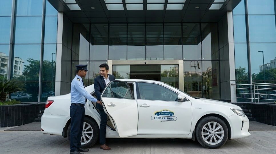a chauffeur opening the door of a premium lord krishna travels sedan for a business executive at a 5 star hotel entrance in noida.